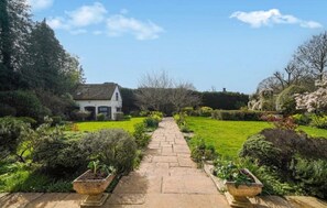 Un chemin menant à une maison entourée d’un jardin bien entretenu, où l’on trouve diverses plantes et arbustes.