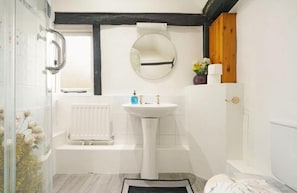 A bathroom with a white sink, a round mirror, a white radiator, and a wooden door.