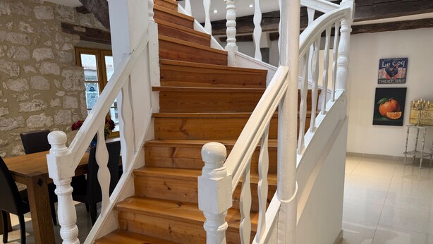 Een houten trap met witte balustrades, een stenen muur en een eethoek met tafel en stoelen.