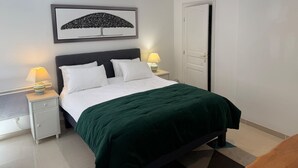 Een keurig opgeruimde slaapkamer met een bed, twee nachtkastjes, een aan de muur hangend schilderij en een deur.