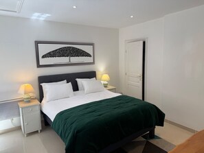 Ein ordentlich eingerichtetes Schlafzimmer mit einem Bett, zwei Nachttischen, einem Wandbild und einer Tür.