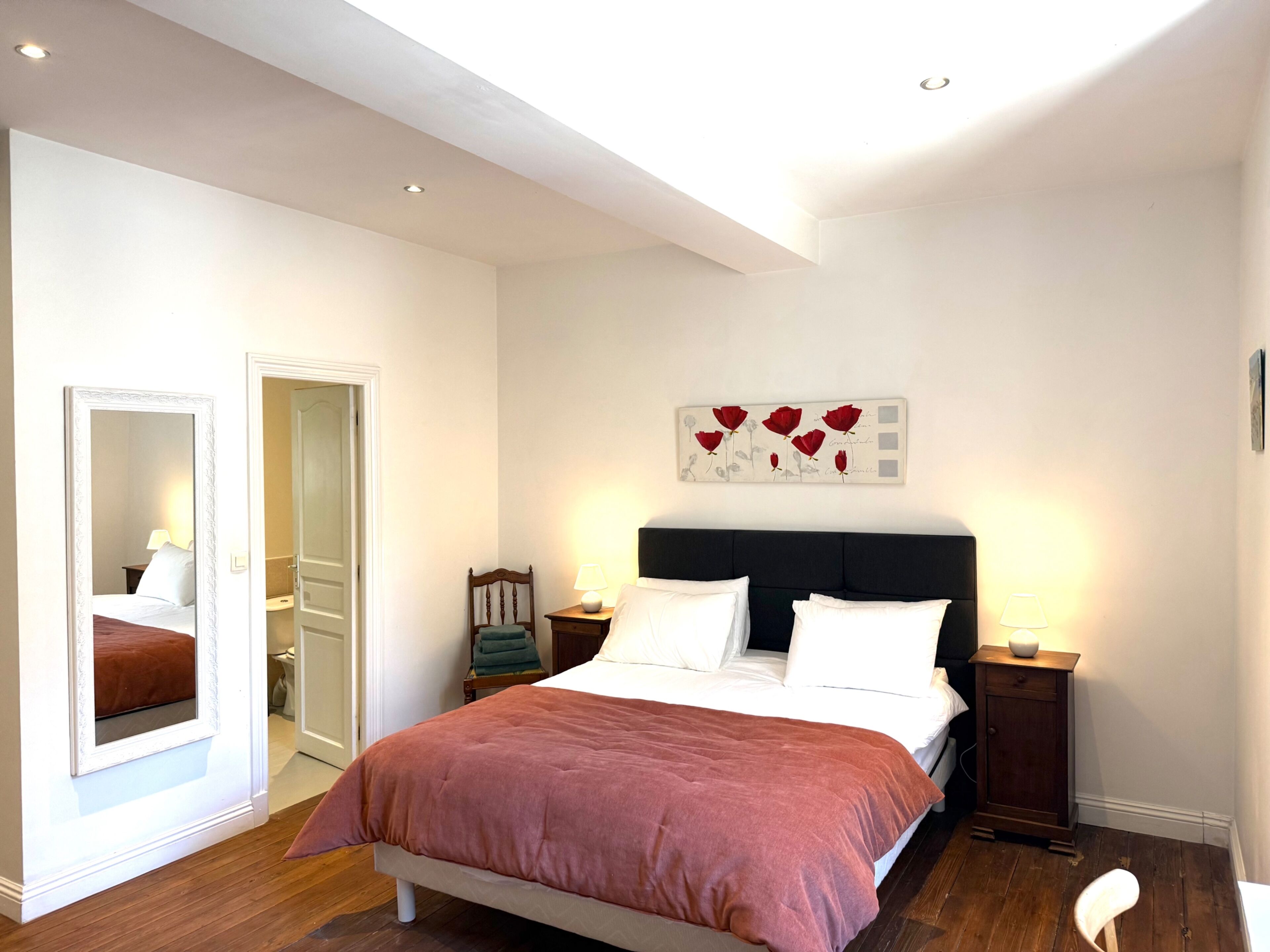 Une chambre à coucher comprenant un lit, un miroir, une table de chevet, une œuvre d’art murale et une porte.