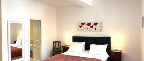 A bedroom with a bed, a mirror, a nightstand, a wall art piece, and a door.