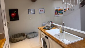 Een keuken met een houten aanrecht, een spoelbak en een wasmachine. Er zijn twee dierenbedjes en kunstwerken in lijsten aan de muur.
