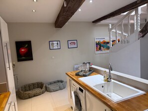 Eine Küche mit einer Holzausziehtheke, einem Spülbecken und einer Waschmaschine. Zwei Tierbetten und gerahmte Kunstwerke sind an der Wand zu sehen.