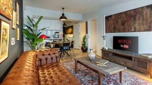 A living room with a leather sofa, a coffee table, and a TV displaying Netflix and YouTube logos. There is a dining area with chairs and a table, and a kitchen in the background. - Panoramic Bosphorus View Terrace At Monnas Suite (Istanbul)
