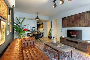 A living room with a leather sofa, a coffee table, and a TV displaying Netflix and YouTube logos. There is a dining area with chairs and a table, and a kitchen in the background. - Panoramic Bosphorus View Terrace At Monnas Suite (Istanbul)