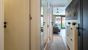 A hallway with a door, a cabinet with plants, a patterned rug, and a view of a living area with a sofa and a hanging light fixture. - Huge Balcony Taksim Rooftop Apt At Monnas Suite (Istanbul)