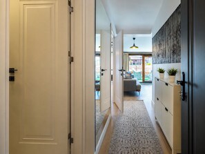 A hallway with a door, a cabinet with plants, a patterned rug, and a view of a living area with a sofa and a hanging light fixture. - Huge Balcony Taksim Rooftop Apt At Monnas Suite (Istanbul)