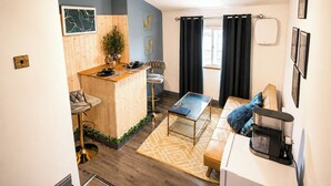 Ett kompakt bostadsutrymme med ett litet kök, en matplats och en sittgrupp med en kaffemaskin.
