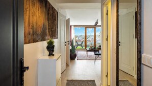 Ein Flur mit Blick auf einen Balkon, eine Pflanze auf einem Beistelltisch und eine Tür zu einem Zimmer.