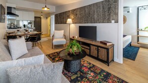 Ein modernes Wohnzimmer mit Sofa, Couchtisch, Fernseher und einer Küche im Hintergrund.