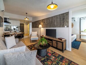 Ein modernes Wohnzimmer mit Sofa, Couchtisch, Fernseher und einer Küche im Hintergrund.