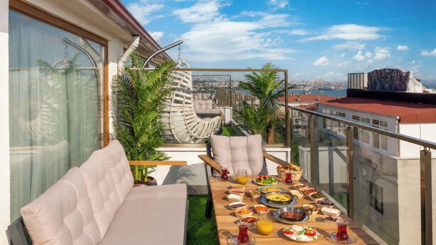 Eine Dachterrasse mit Esstisch, gedeckten Plätzen für das Frühstück, bequemen Sitzgelegenheiten und Blick auf die Stadtlandschaft.