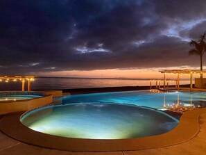 Zona de piscina amb vistes a l'oceà al capvespre, envoltada d'una terrassa de fusta i llums de garlandes.