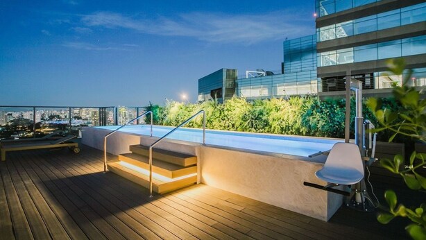 Terraço no telhado com piscina, escadas e um edifício moderno ao fundo.