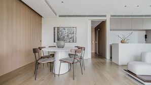 Uma sala de jantar moderna com uma mesa redonda e cadeiras, uma grande pintura abstrata e uma cozinha com bancada branca e um vaso.