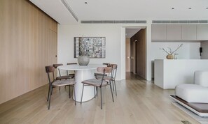 Ein moderner Essbereich mit einem runden Tisch und Stühlen, einem großen abstrakten Gemälde und einer Küchenzeile mit weißer Arbeitsplatte und einer Vase.