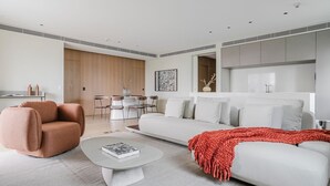Uma sala de estar moderna com sofá, poltrona, mesa de centro e área de jantar com cadeiras e mesa.