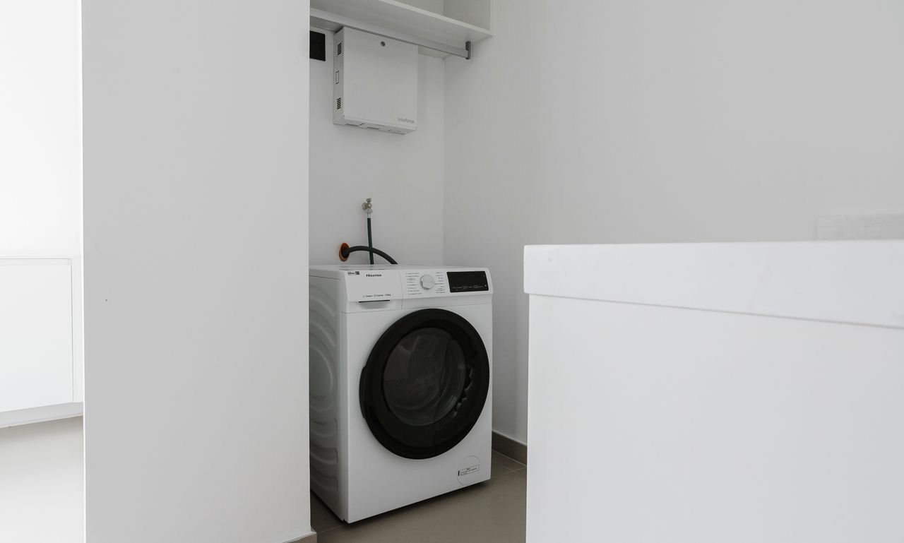 Ein kleiner, weißer Waschraum mit einer Frontlader-Waschmaschine und einem darüberliegenden Schrank.