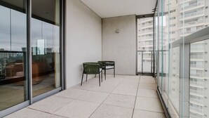 Varanda com porta de vidro, duas cadeiras e vista para a cidade.