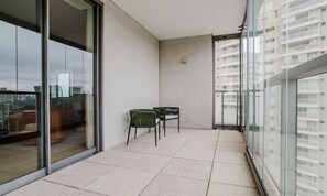 Ein Balkon mit Glastür, zwei Stühlen und Blick auf eine Stadtansicht.