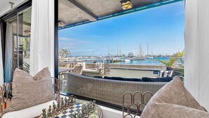 Een balkon met een schaakbord, rieten meubilair en uitzicht op een jachthaven met boten.