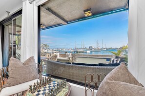 A balcony with a chessboard, wicker furniture, and a view of a marina with boats. - Gorgeous Balboa Island Home, Right on the Bayfront (Newport Beach)