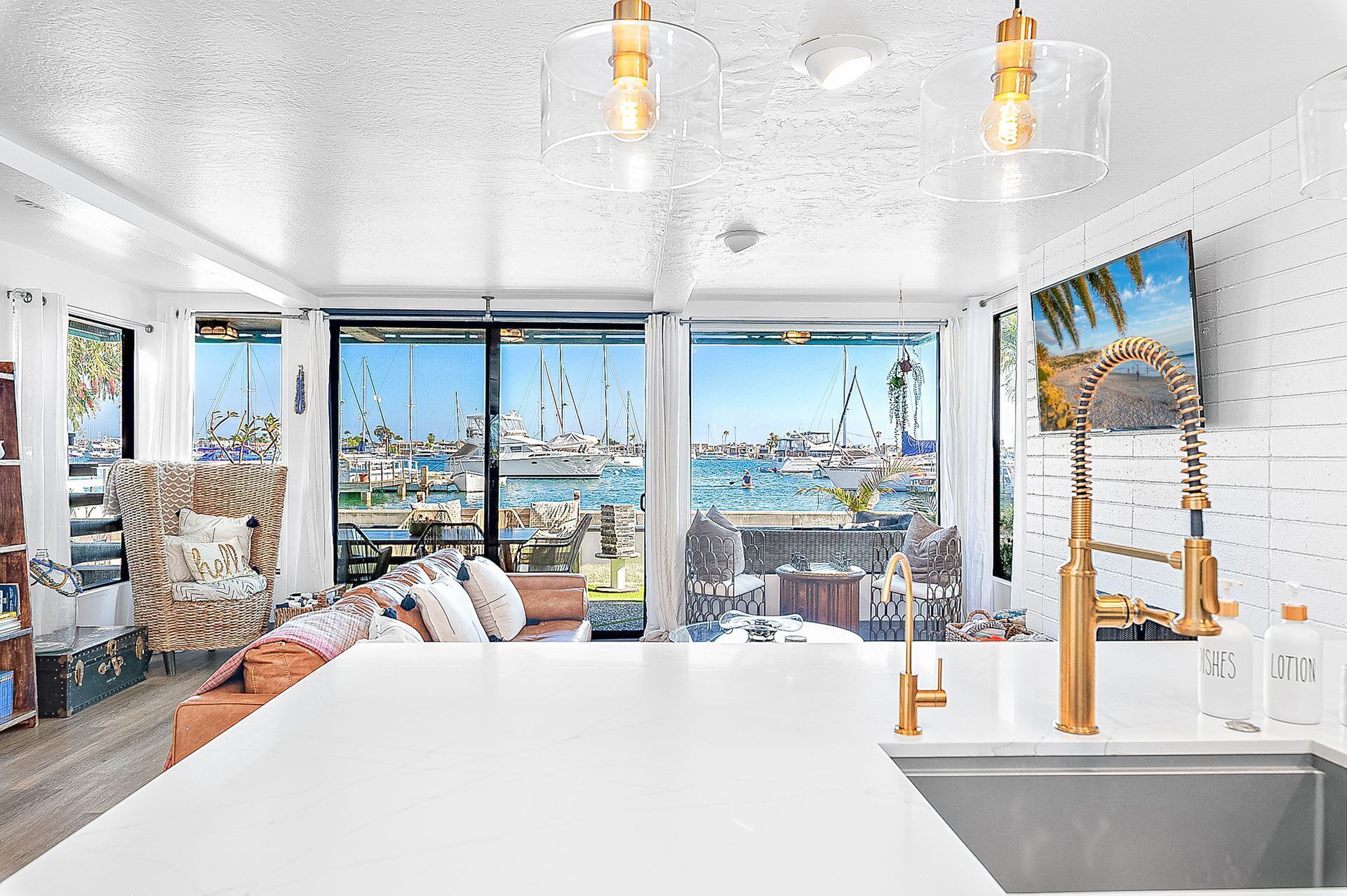 Una cucina moderna con una grande isola, un'area pranzo con mobili in vimini e vista su una marina attraverso ampie finestre.