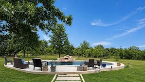 A backyard with a swimming pool, outdoor furniture, and a stone fire pit.