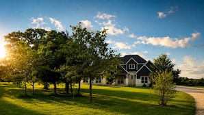 A two-story house with a dark roof, stone foundation, and a driveway leading to the front door.