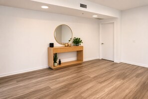 A room with a wooden console table, a round mirror, a potted plant, and a door. - Modern Marina Del Rey 2BR Pool, Gym, Parking, Near Beach (Los Angeles)