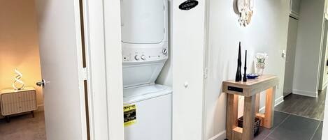 Pesuhuone, jossa on valkoinen kuivausrumpu, pieni pöytä maljakolla ja kyltti, joka kertoo huoneen käyttötarkoituksen.