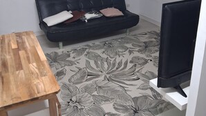 Una stanza con un divano in pelle nera, un tavolo di legno, un televisore su un mobile e un tappeto con motivo floreale.