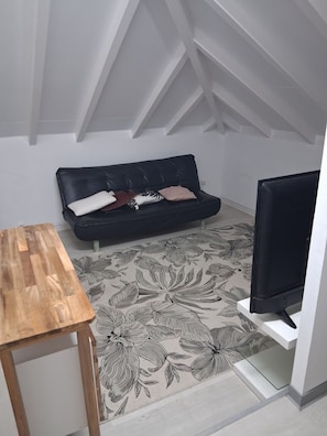 Ein Zimmer mit einer schwarzen Ledersofa, einem Holztisch, einem Fernseher auf einem Schrank und einem Teppich mit Blumenmuster.