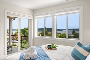A bedroom with a large bed, a view of a lake, and a balcony. - Modern Hilltop Home Lake Views ~ Decks & Patio! (Seattle)