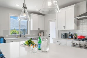 Una cocina moderna con armarios blancos, una isla grande con una jarrón y vasos, y una estufa.