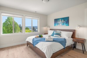 Un dormitorio con un ventanal grande, una cama, una mesita de noche y un cuadro.