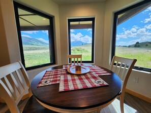 Ein runder Esstisch mit Untertasse, zwei Stühlen und Blick auf ein grasbewachsenes Feld sowie Berge.