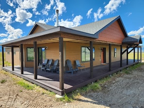 Ein modernes Gebäude mit überdachter Terrasse, Sitzgelegenheiten im Freien und Blick auf die Landschaft.