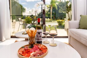 Ein Esstisch mit einer Wurst- und Käseplatte, einer Weinflasche und Gläsern, mit Blick auf einen Garten.