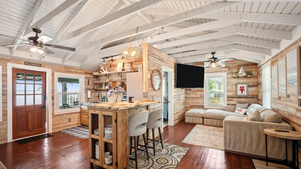 A spacious living area with a wooden ceiling, a kitchen with a bar, and a cozy seating area. - 3-BR Waterfront, Sebastian Inlet Views, Private Dock & Daily Wildlife Sightings (Micco)
