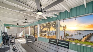 A covered outdoor seating area with a view of the sunset over water, featuring a table and chairs, ceiling fans, and hanging lights. - 3-BR Waterfront, Sebastian Inlet Views, Private Dock & Daily Wildlife Sightings (Micco)