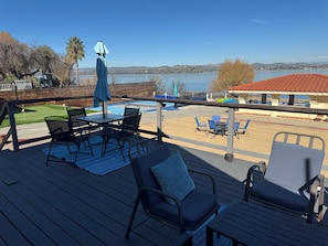 A deck with outdoor furniture, a view of a lake, and a building with a red roof in the background.
