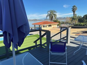 Una terraza con una silla y una sombrilla, una piscina y vistas de un edificio con techo rojo.