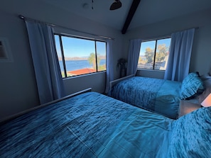 Una habitación con dos camas, ventanas amplias, ventilador de techo y vista a un cuerpo de agua.