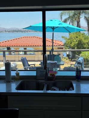 A kitchen with a view of the sea, a patio with chairs, and a sign that says 'ENJOY the LITTLE THINGS.' - Lakefront Oasis with 2 Private Pickleball Courts, Kayaks, Gazebo, Games & BBQ (Lake Elsinore)