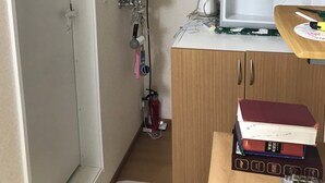 Una cocina compacta con microondas, un refrigerador pequeño y un lavamanos. Se observan gabinetes de madera, una encimera con algunos objetos, y una puerta que da a otra habitación.