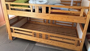 Una cama nido de madera con un ventilador y almohadas, un estante de madera y suelo alfombrado.