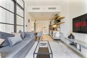 Ein modernes Wohnzimmer mit einem grauen Sofa, einem Couchtisch, einem Fernseher mit Netflix-Logo und einer Küche im Hintergrund.
